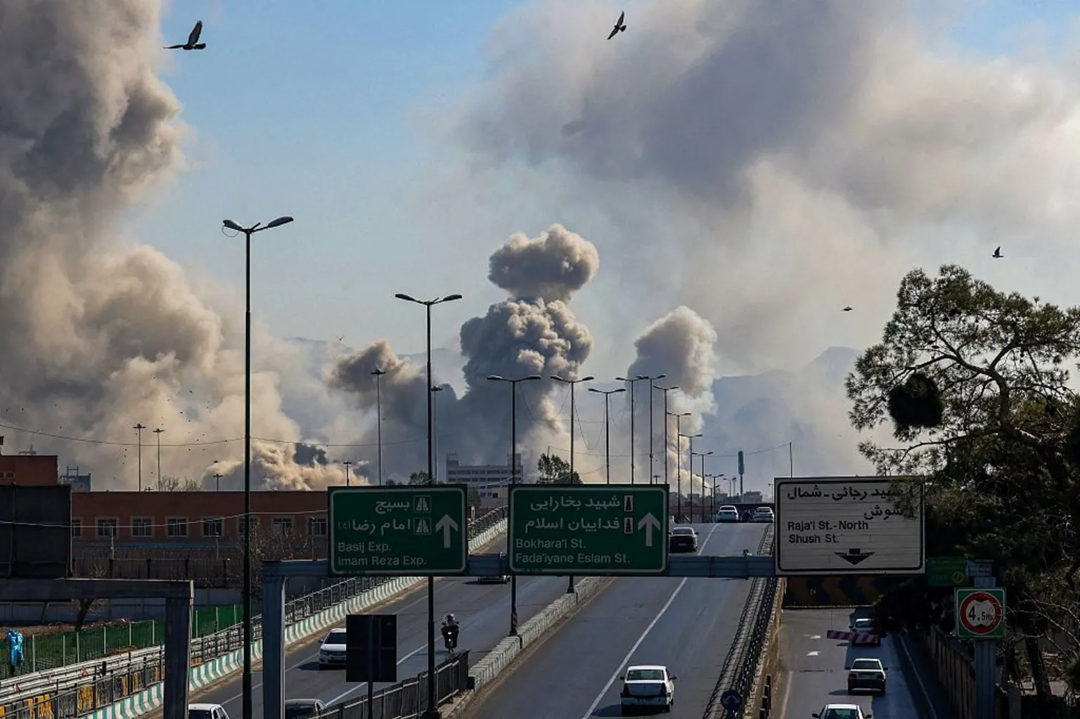 AFP via Motorists drive along an expressway as plumes of smoke rise after a strike in Tehran on 5 March 2026.