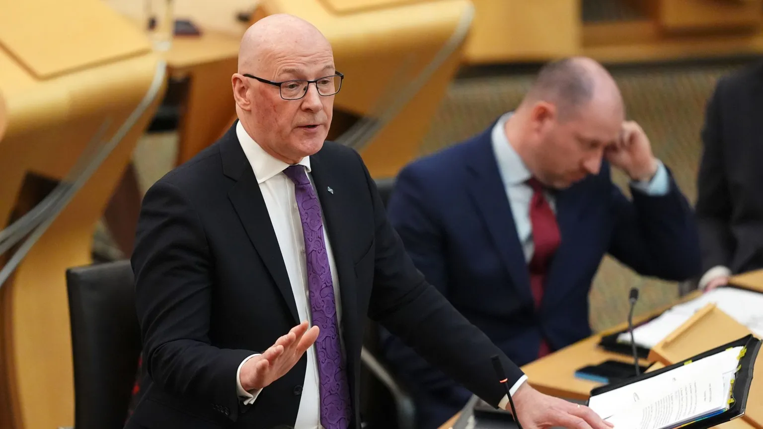  A bald man with glasses wearing a dark suit and a purple tie