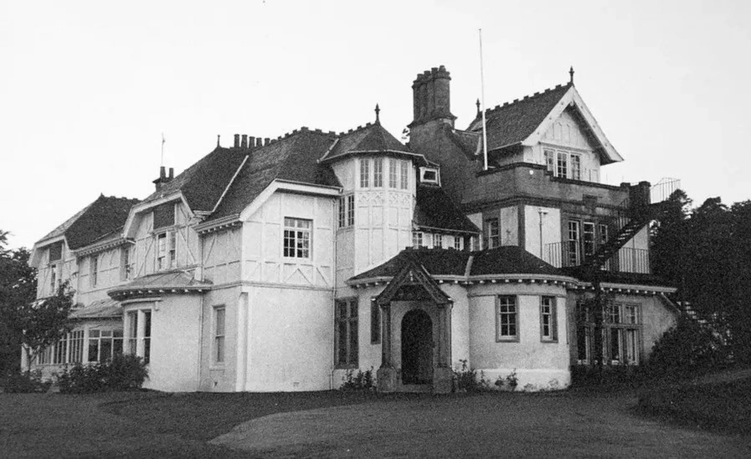 Black and white image of a large white Victorian-style home. 