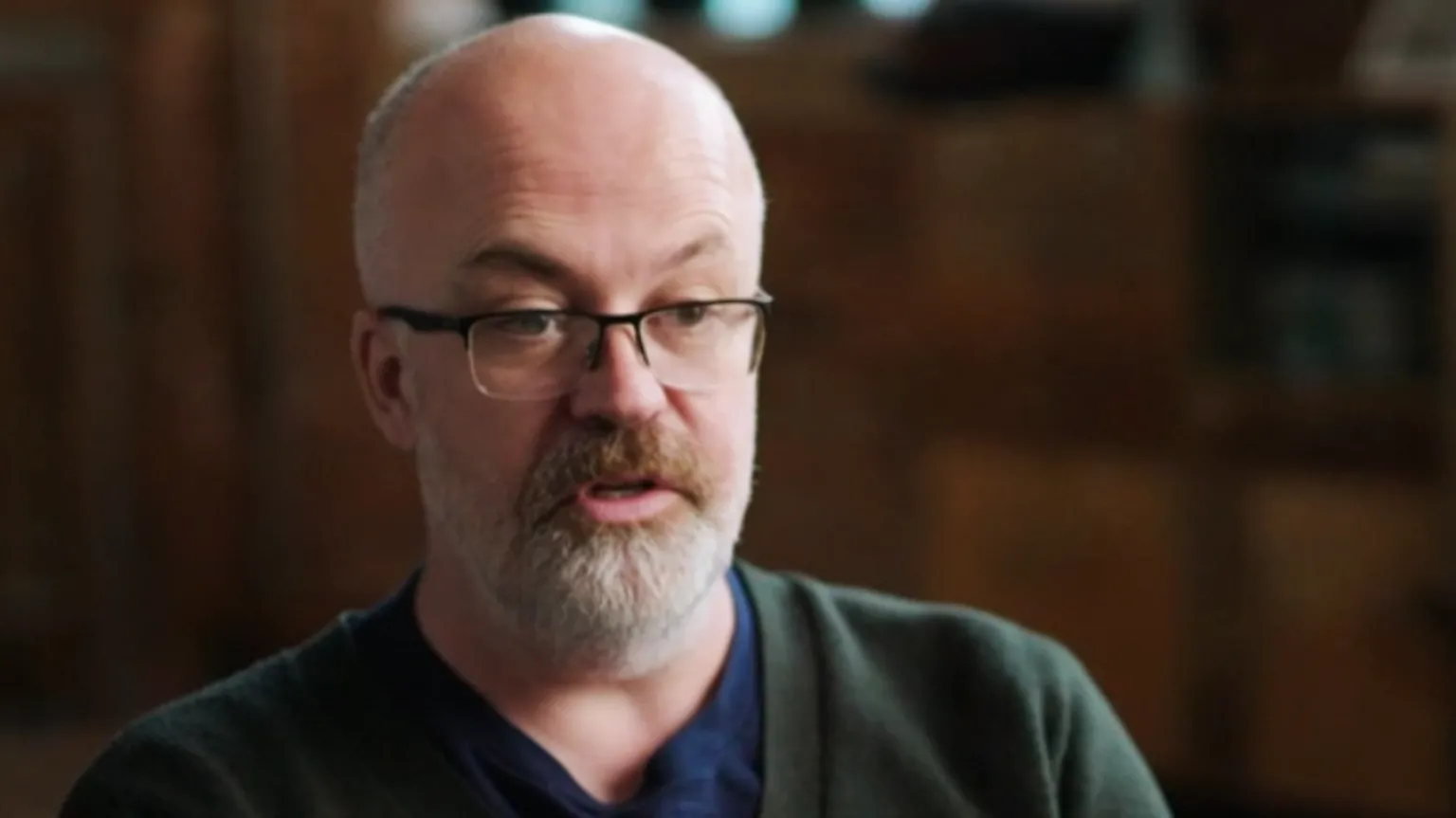 Andrew Morgan, a bald man with glasses and a beard. He is wearing a green cardigan over a dark blue top.