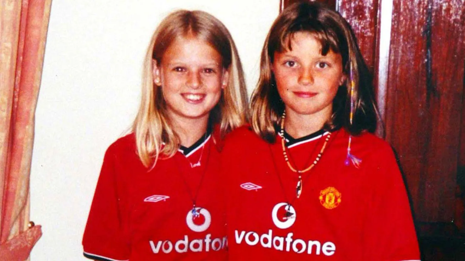  Holly Wells, pictured on the left, and Jessica Chapman, who is on the right, are wearing red Manchester United football shirts and smiling towards the camera. Holly is blonde and Jessica has light brown hair.