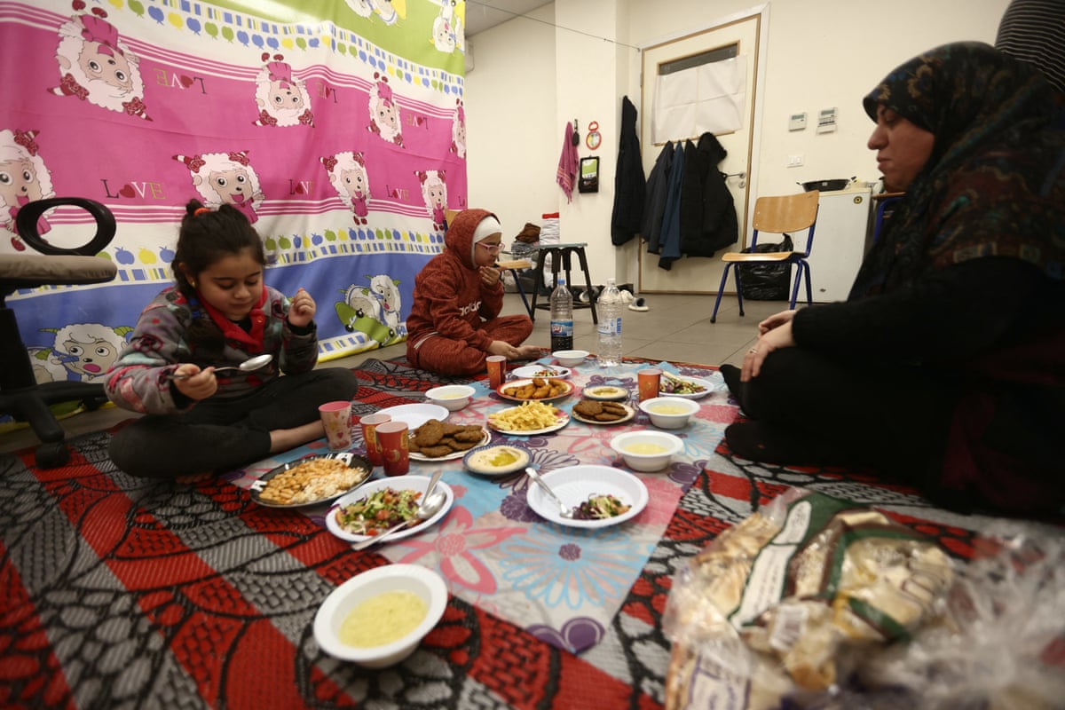 a woman eats a meal with her two children on the floor of a classroom