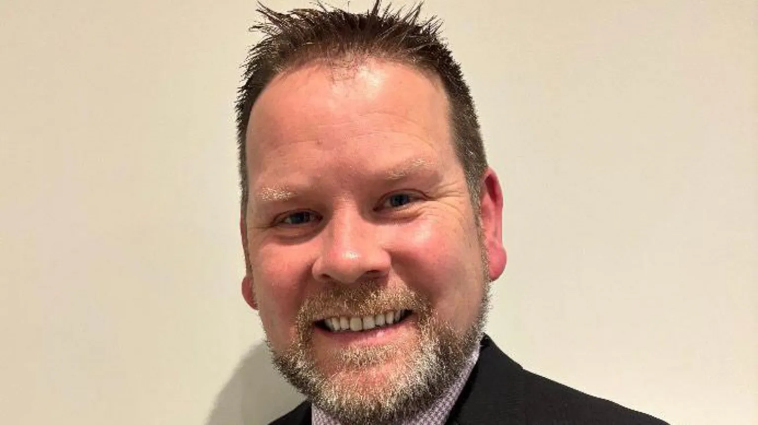 David Thompson David Thompson. He has short brown hair spiked up and a beard. He is wearing a dark blazer and a check shirt. He is smiling at the camera.