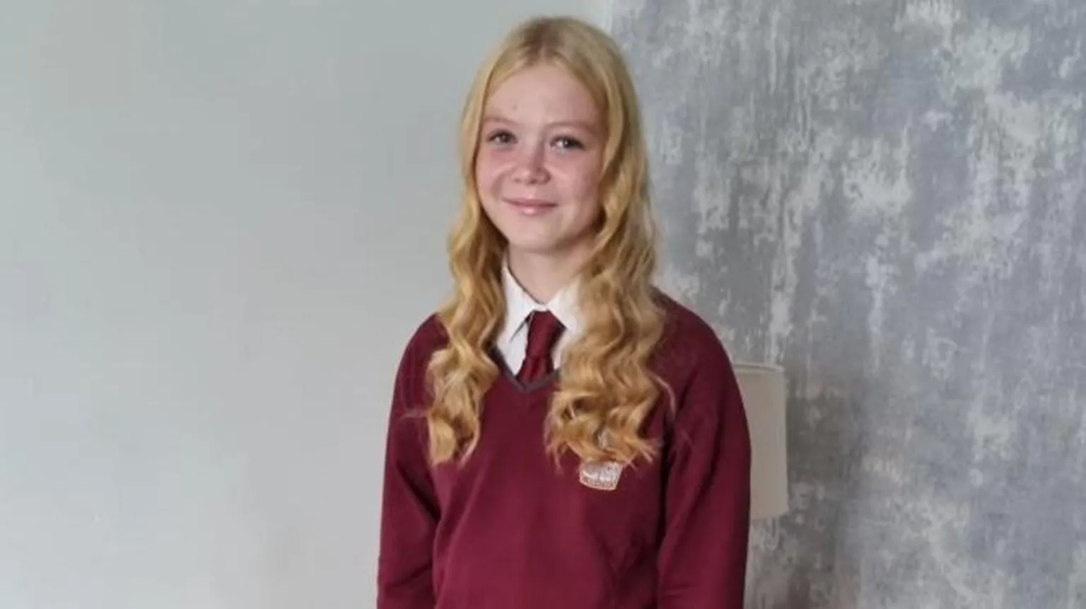 Family photo A schoolgirl in maroon tie and jumper is looking at the camera and smiling. She has long blonde hair which is wavy.