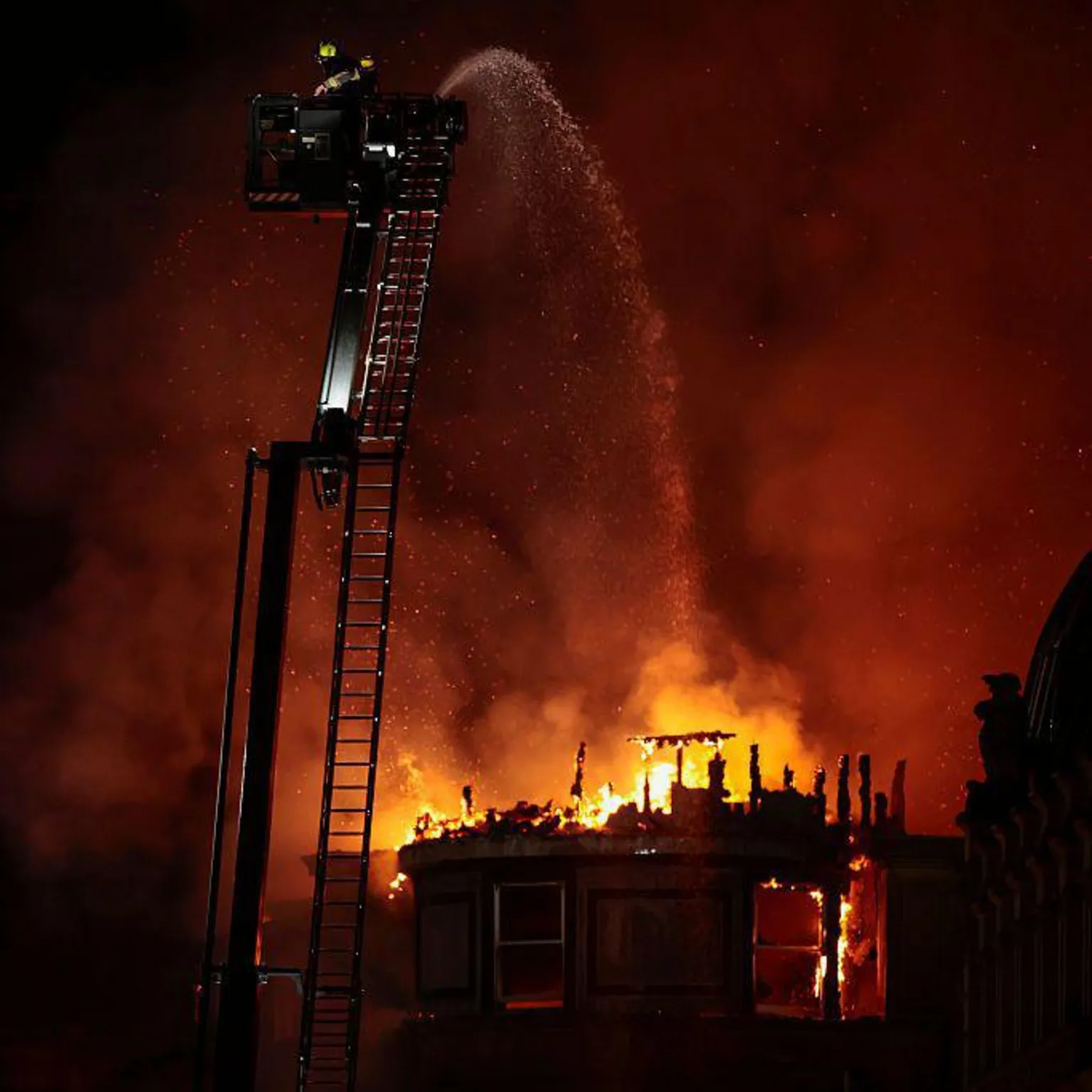  A burning and destroyed building, with firefighters on an extendable ladder spraying water over it