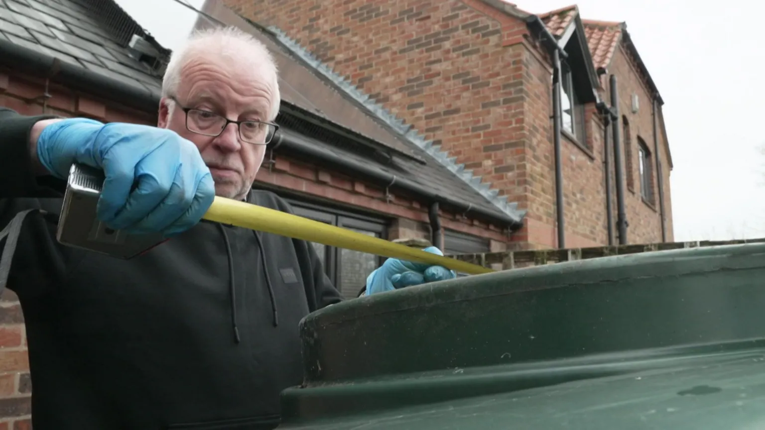 Bob Hayes, who has grey hair and black-rimmed glasses, uses a tape measure to check the oil level in his tank.