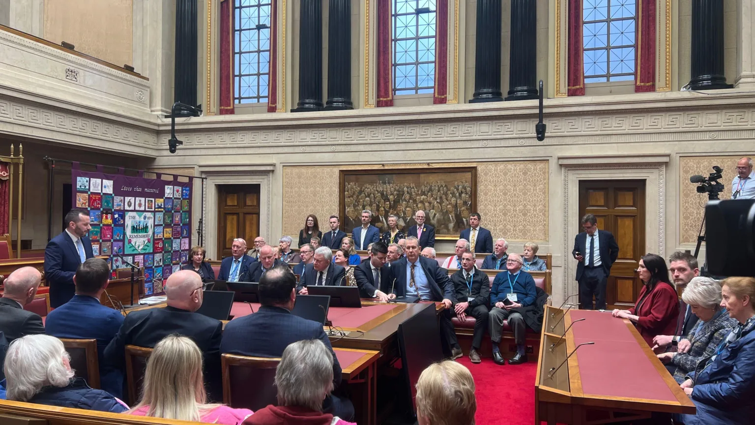 People sitting in Stormont buildings. A man is speaking at the front of the room.