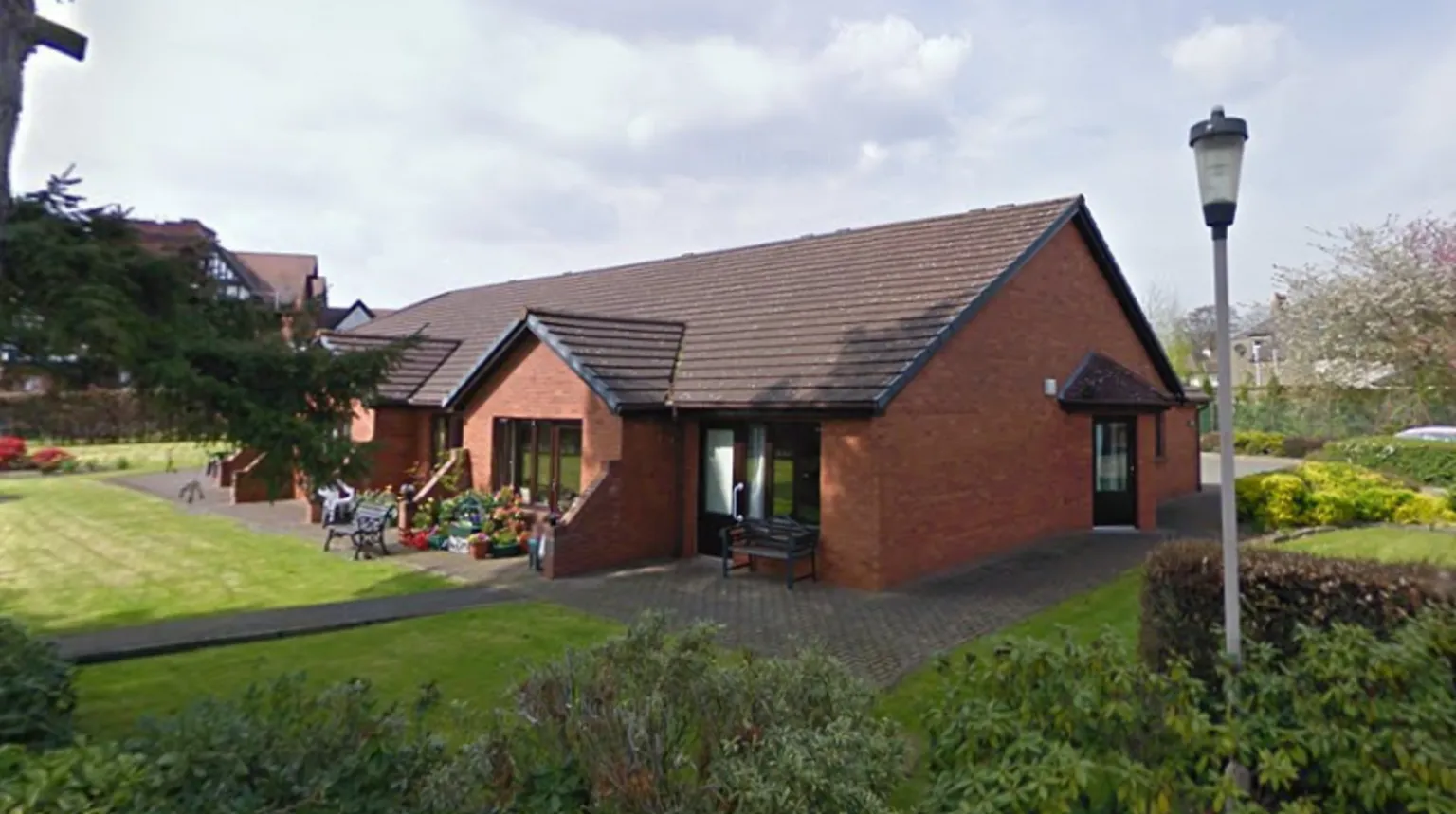 Google A single-storey red brick building with a surrounding garden