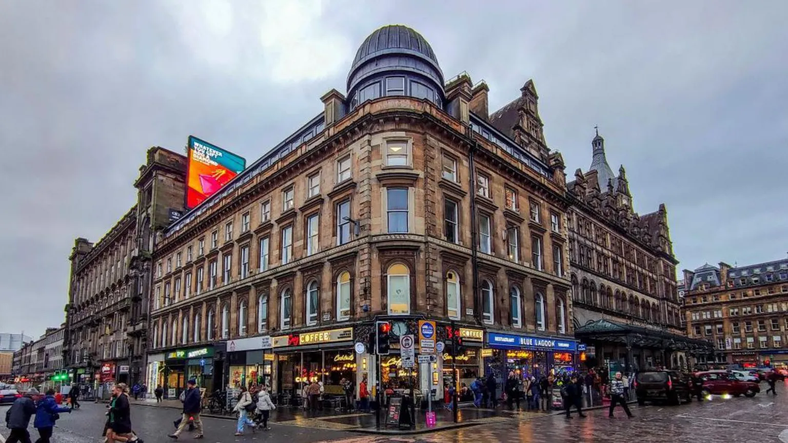  Union Corner before the fire. The Victorian building has a domed roof on the corner and shops along the ground floor. People walk on the pavement in front of the buildings.