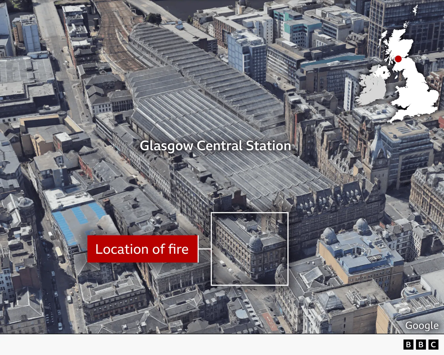A 3D image, generated from satellite images, showing Glasgow Central Station and the building in the same block which was on fire overnight. We are looking in a south-west direction from above the city at a satellite image from 2024. The building which was on fire is situated right next to the main entrance of the station on the corner of a long, unbroken row of buildings running up the east side of the station building parallel with the tracks. The five-storey, stone building has multiple retail spaces at ground level extending south and west from the crossroads and a grey dome on the corner of the building rises above the slate roof. The 19th century Grand Central Hotel next door, which forms the northern facade of the train station, is two storeys taller with a high gabled roof full of windows protruding from the garret rooms. Behind the hotel the huge glass roof of the station, formed of multiple smaller glass peaks running in parallel with the tracks. It covers all the platforms, with the train tracks seen curving out of station at the top of the image.