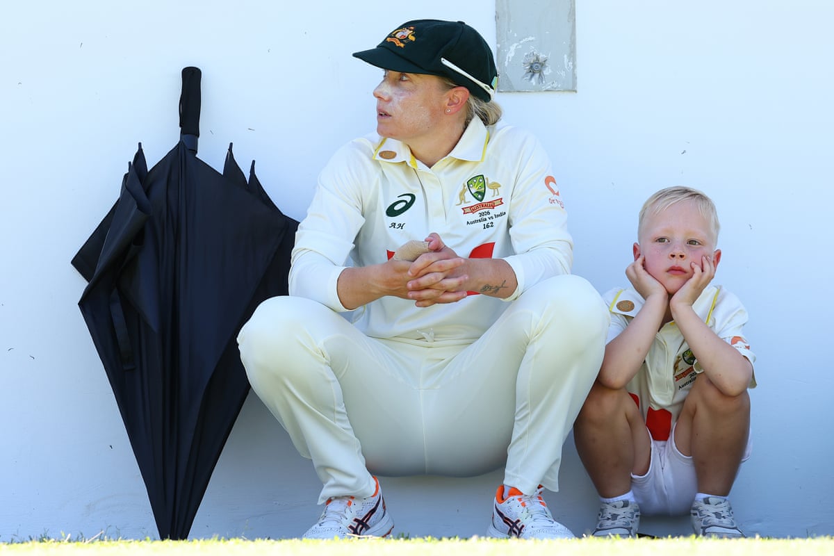 Healy and her nephew crouch leaning against a white wall next to a black umbrella