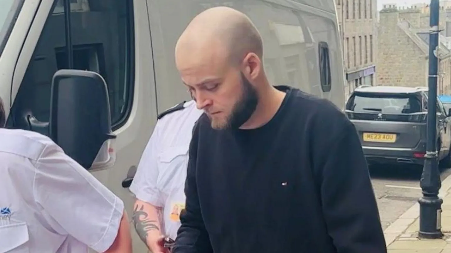 Josh Buchan being led from court in handcuffs to a waiting prison van, he has a bald head and a beard and is wearing a dark jumper.