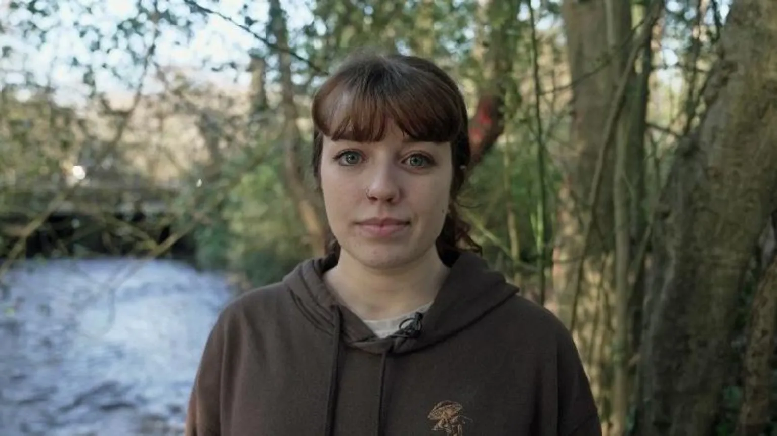 Molly Hadley wears a brown hoodie, grey t-shirt and has her dark brown hair tied up in a ponytail