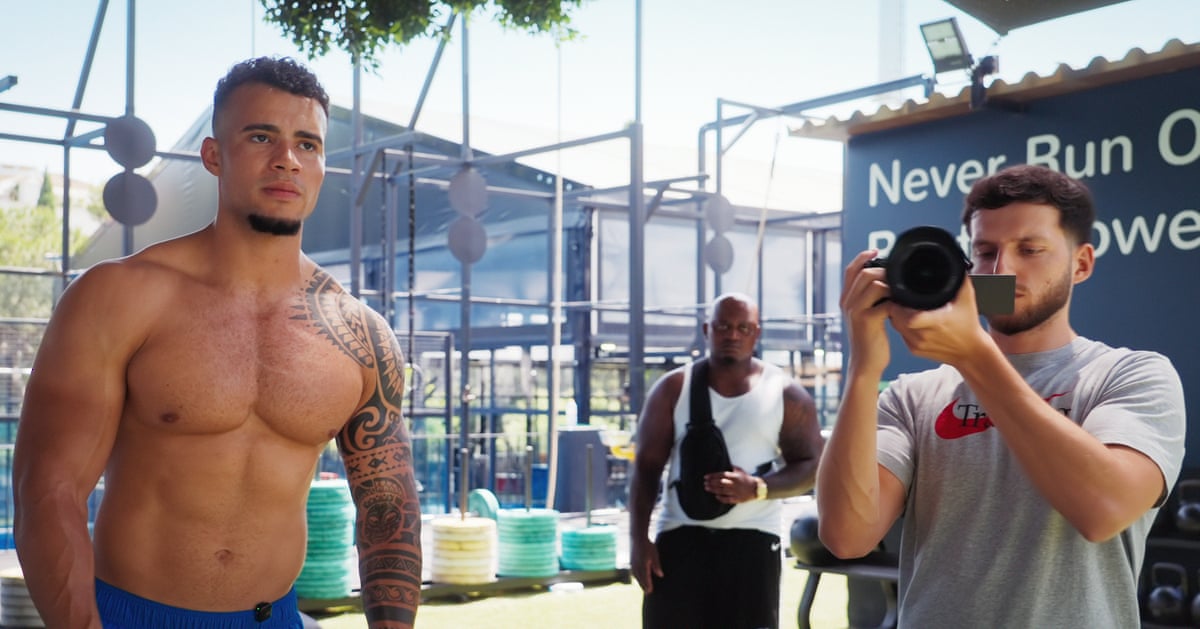 A bare chested Harrison Sullivan and a member of the film crew holding a camera