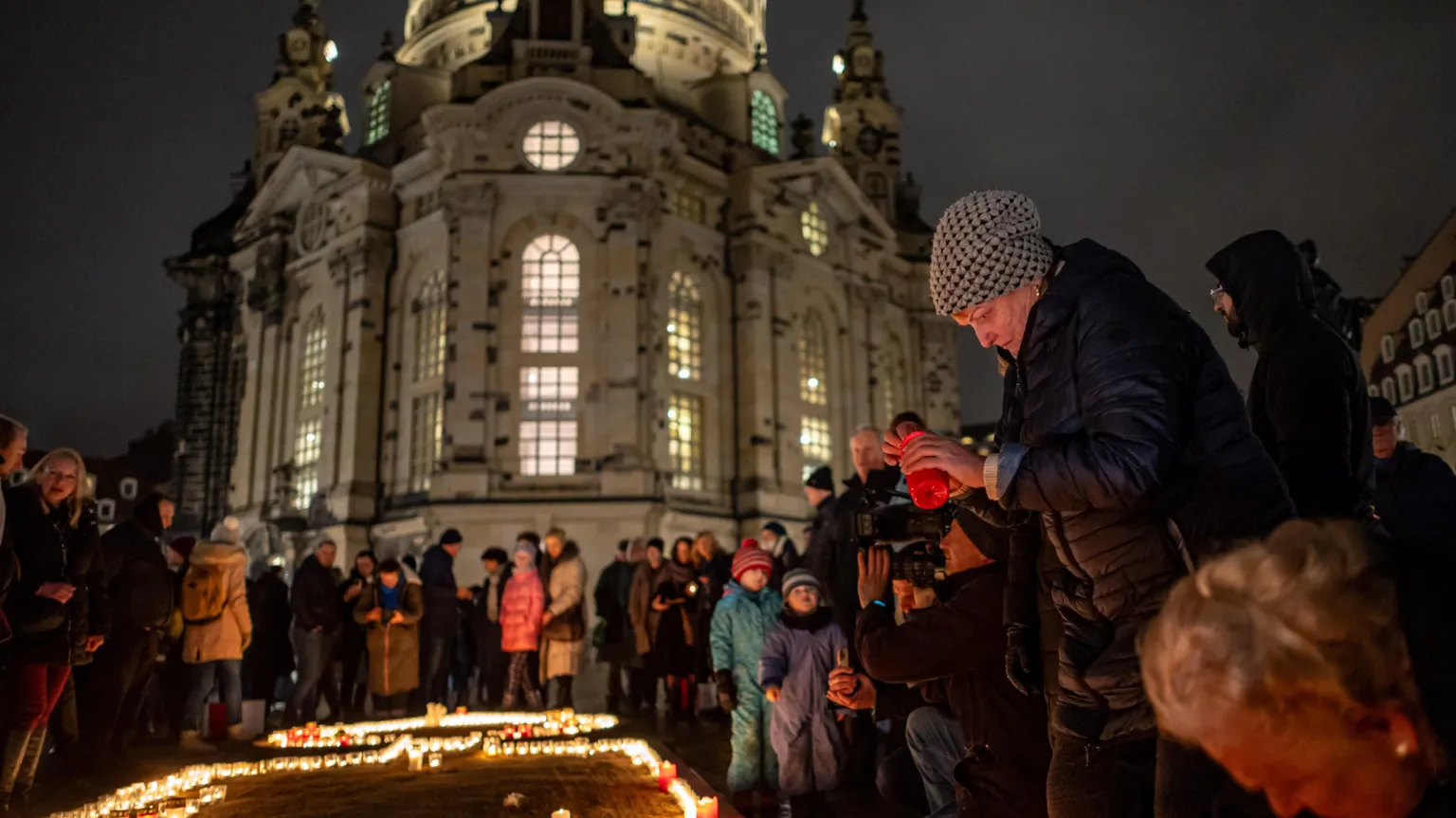 EPA Woman in a woolly hat lights a candle as crowds gather round an array of candles on the ground. Behind them looms the Frauenkirche Lutheran church