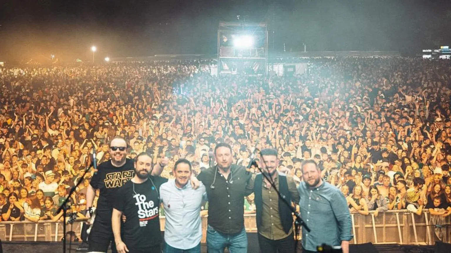 Oscar Bradley The band standing next to each other on stage with the crowd behind him.