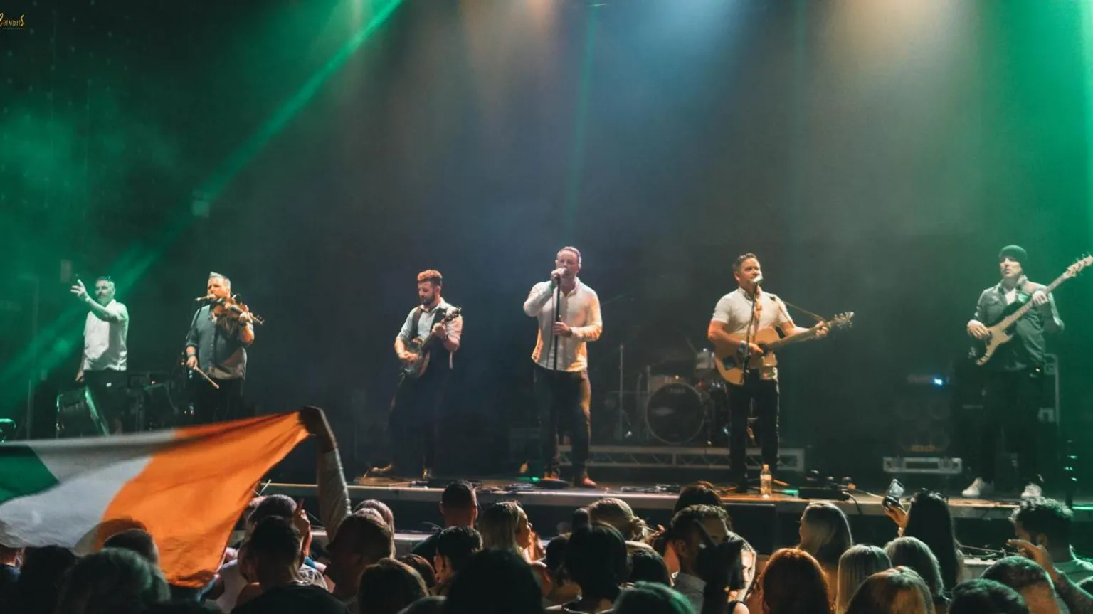 Oscar Bradley The band performing on the stage in front of a crowd of people. The lighting is green. 