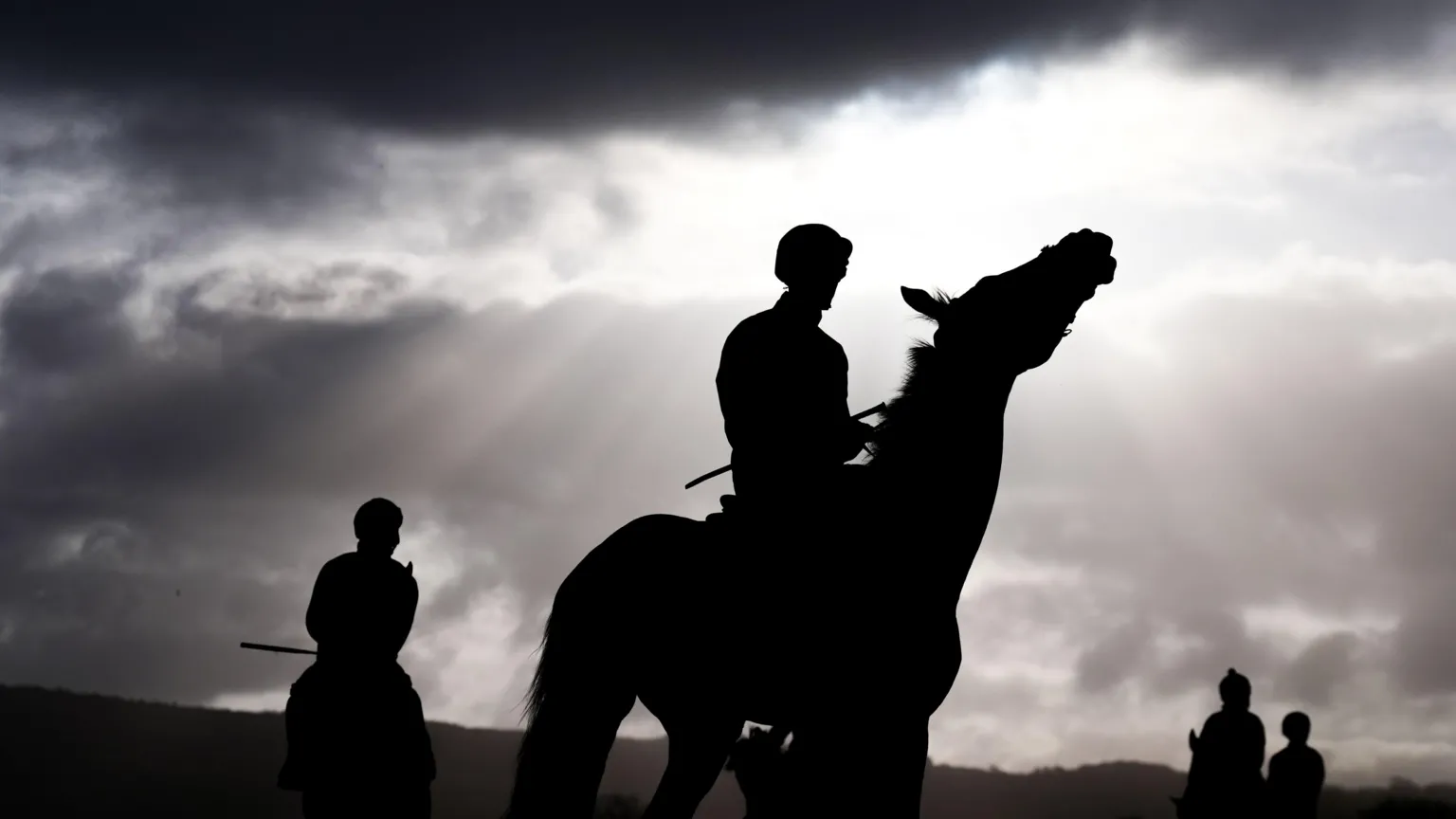 A horse and rider are silhouetted against a bright sky early in the morning on day two of the Cheltenham Festival 2026