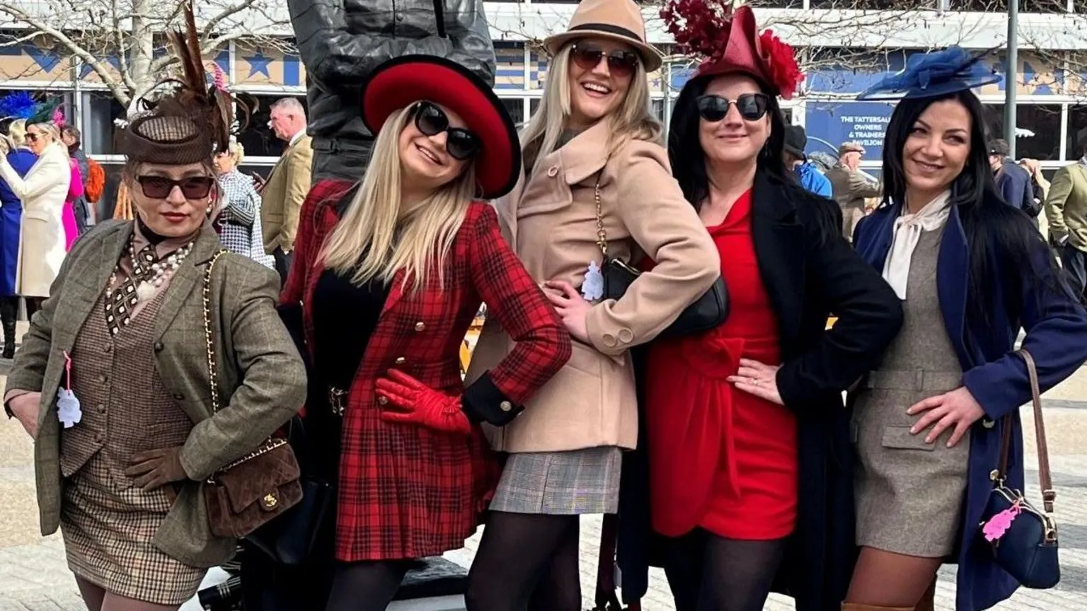 Five young women pose with their hands on their hips side on to the camera. They are all wearing tweed or smart jackets and dresses with hats and fascinators.