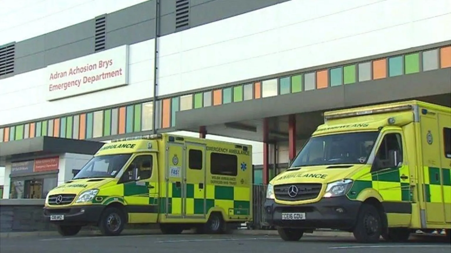 Outside of Glan Clwyd A&E department with two ambulances parked outside. The white-clad building has a row of colourful tiles running along the bottom of it. 