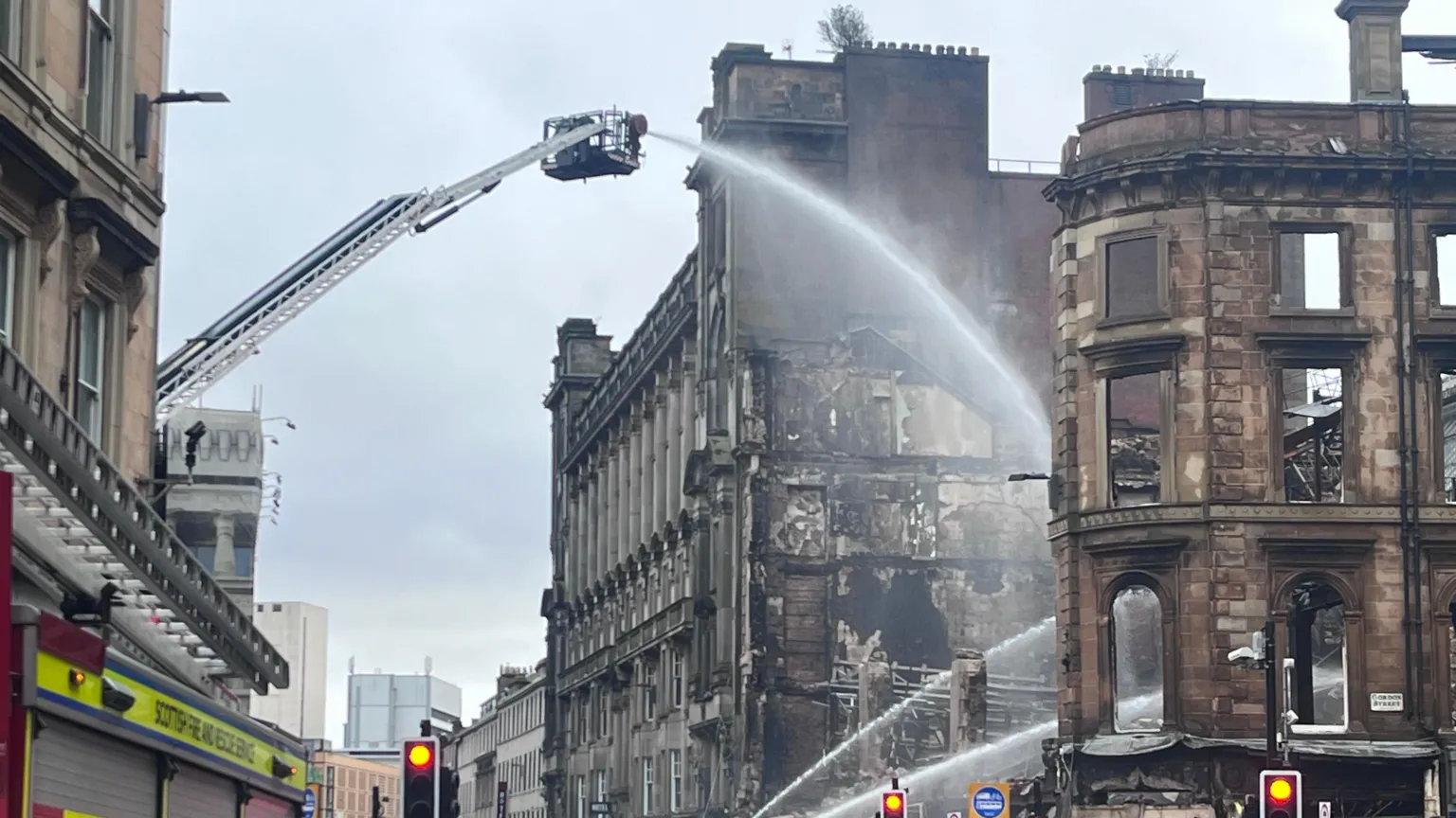 A burned out building in Glasgow, showing the damage from a fire. Fire engines spray water over the ruins.