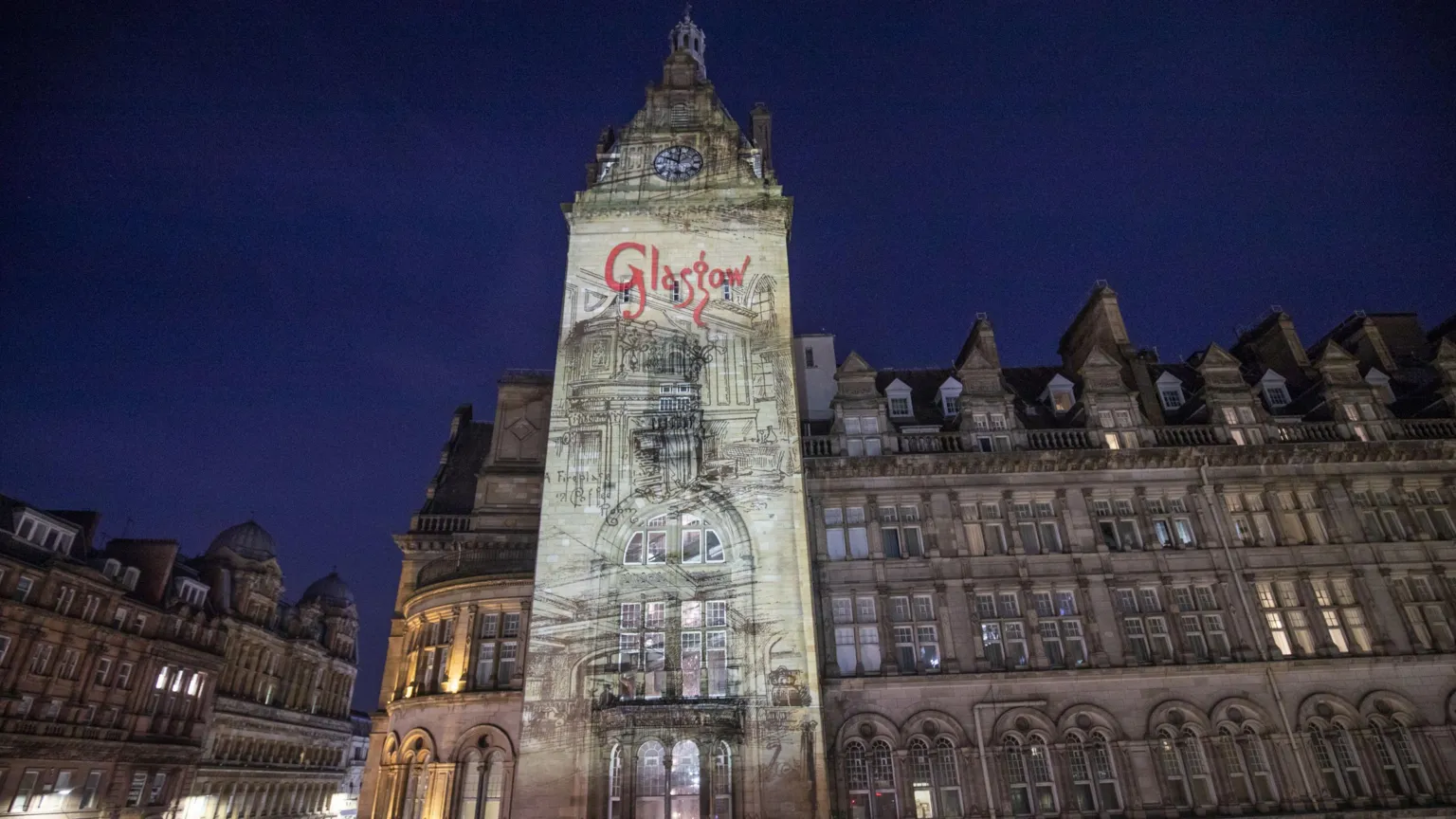 A large Victorian era hotel building in Glasgow, with a light showing shining over it. GLASGOW is spelled out in red.