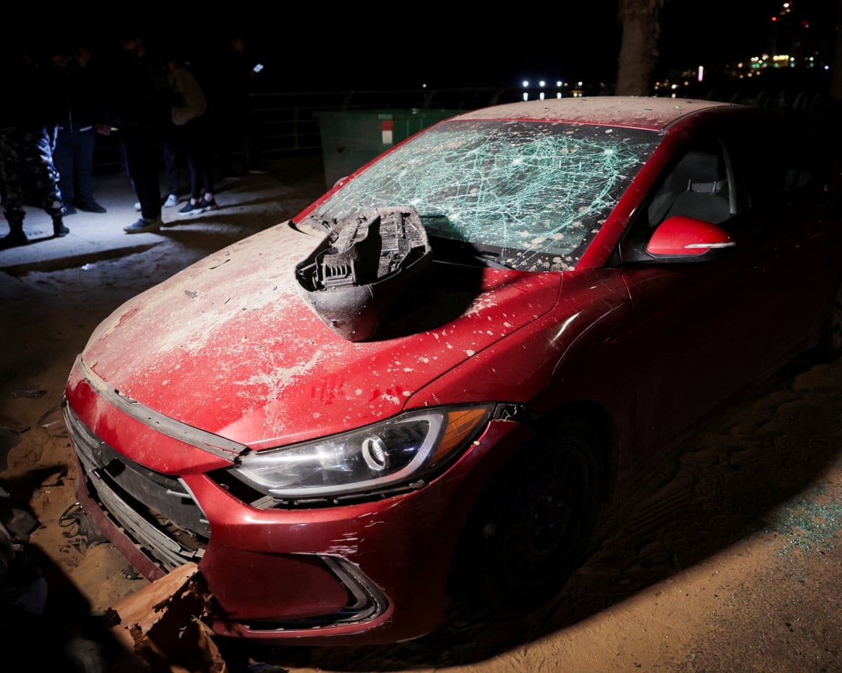 People gather next to a damaged car at the scene where a drone strike targeted another vehicle in Ramlet al-Baida at Corniche Beirut in the Lebanese capital
