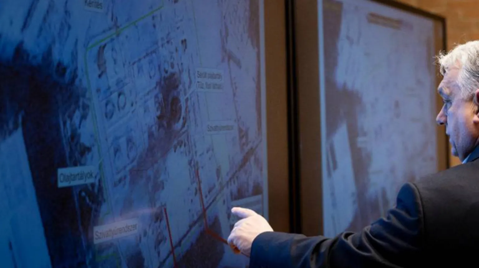 Hungarian government Viktor Orban pointing to a satellite image showing some red lines with his left-hand finger