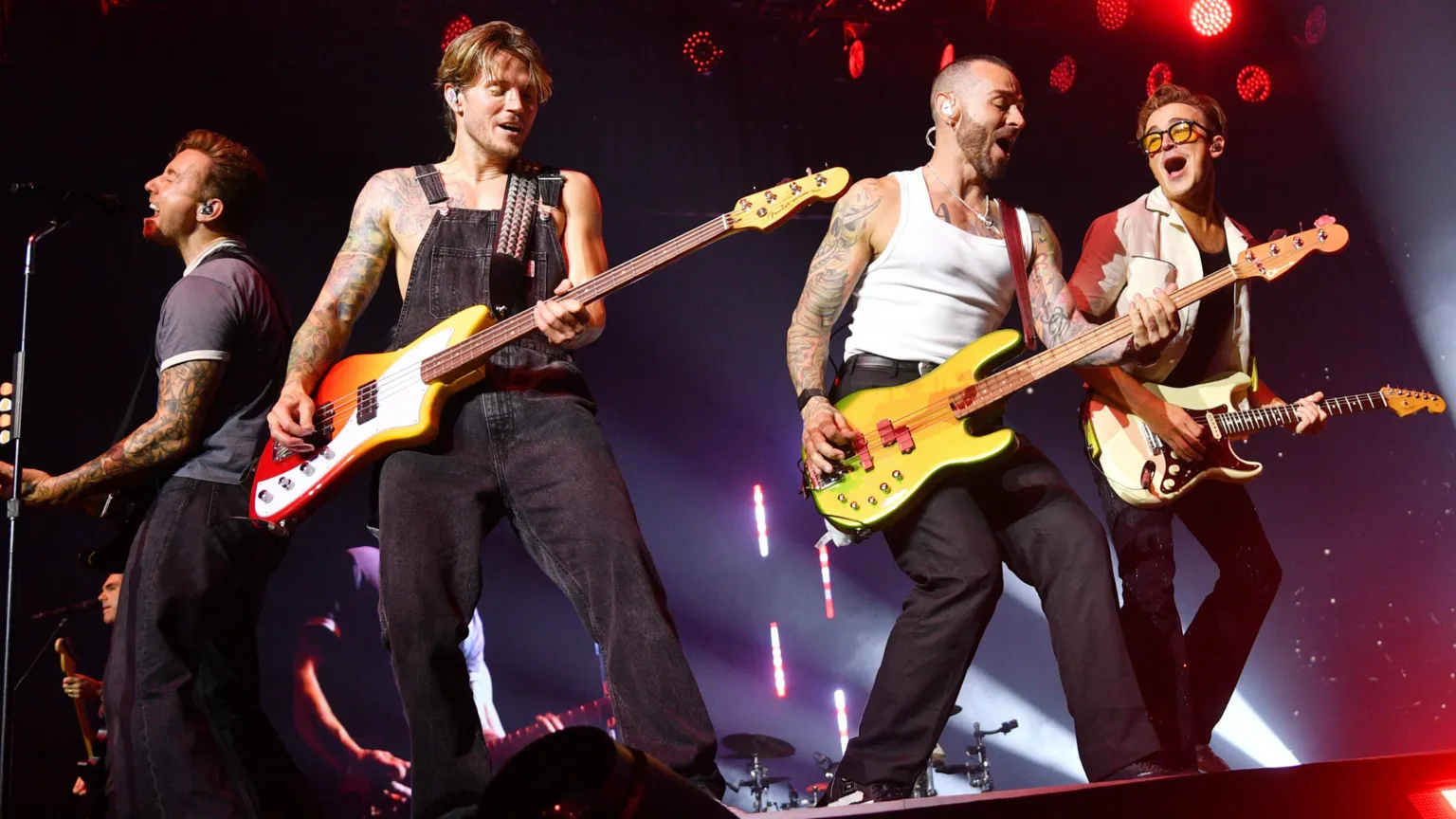 L-R- Danny, Dougie, Matt, Tom Dougie, Matt and Tom are playing electric guitars. Danny is standing in front of a mic singing, wearing blue trousers and blue striped shirt. Dougie wears black dungarees. Matt is wearing black jeans and a white vest. Rom wears all black with a white jacket.
