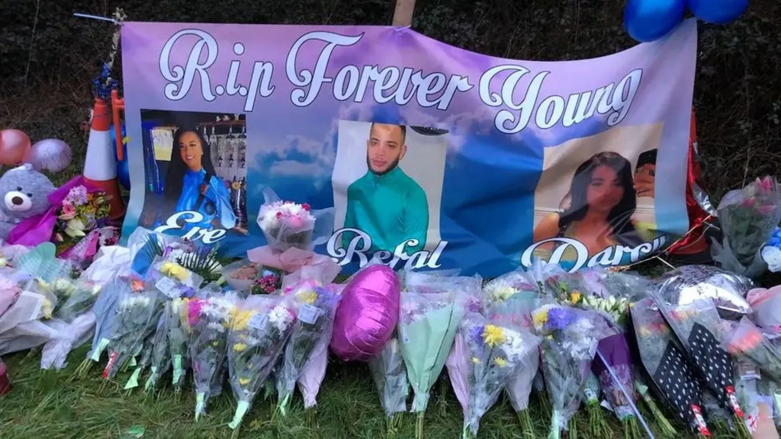 Floral tributes in front of a banner reading: R.I.P Forever Young. That is followed by photos and the names of the three people that died in the crash