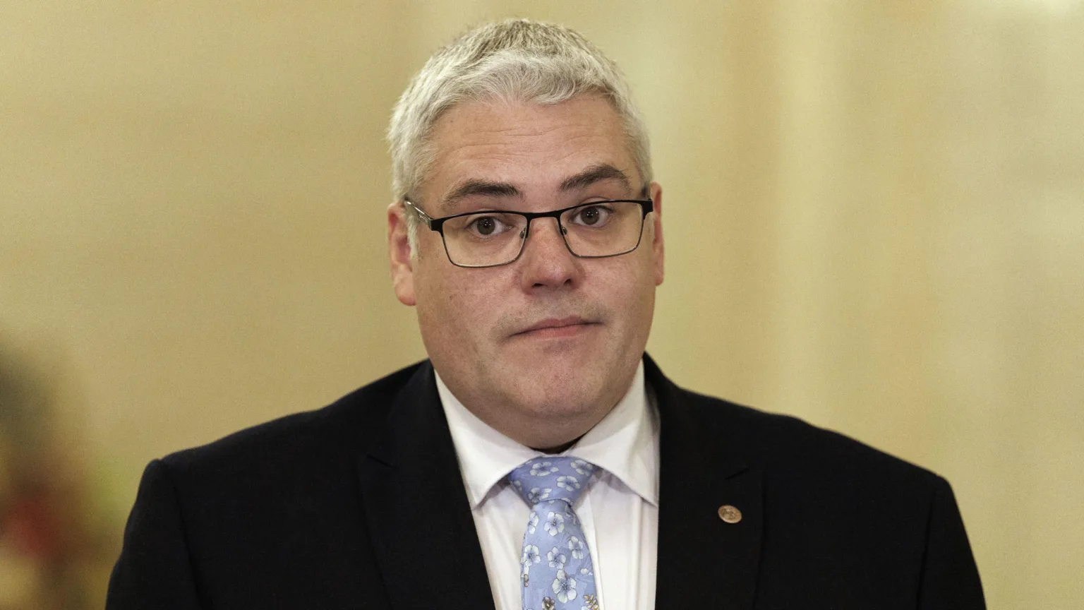 Gavin Robinson, a man with grey hair, wearing glasses in dark suit, white shirt and blue patterned tie.