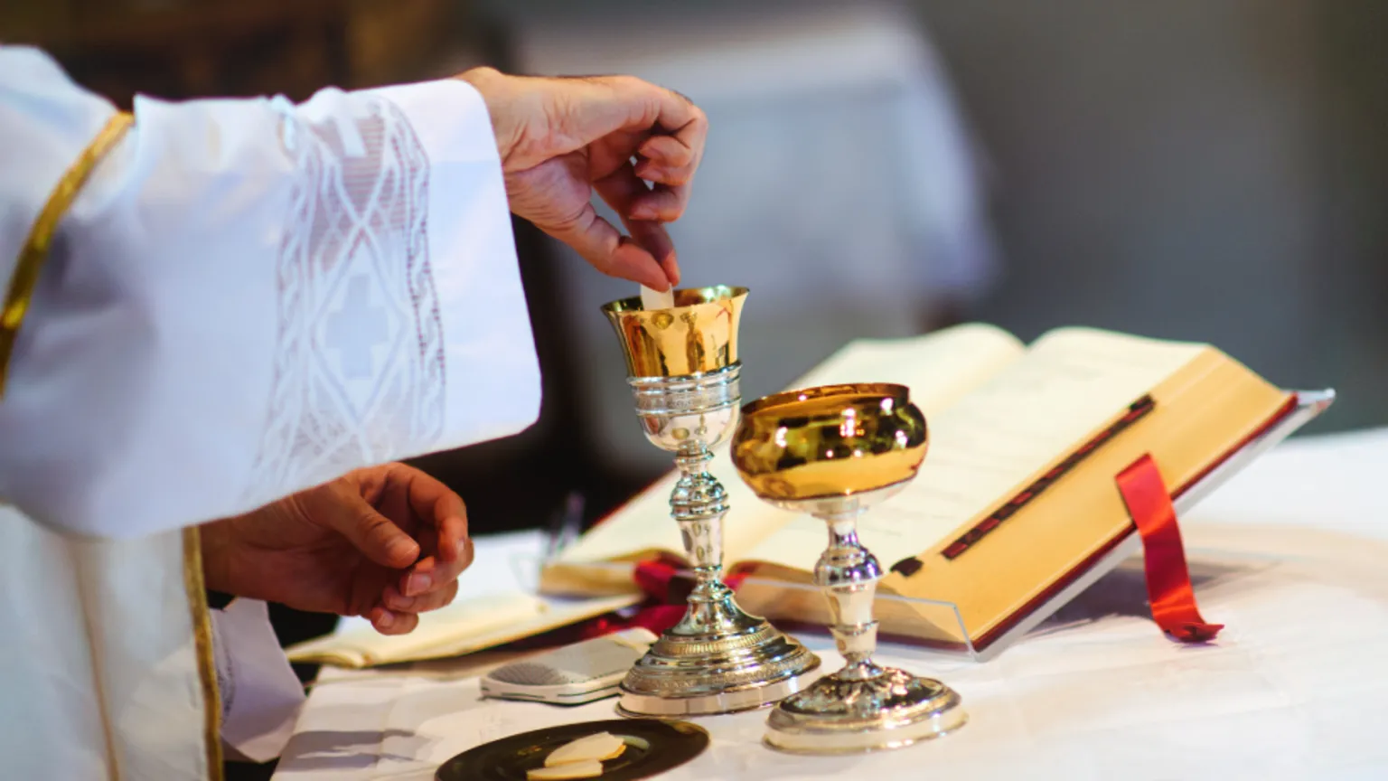  An alter with a hand dipping communion bread into a goblet of wine, and an open bible open behind.