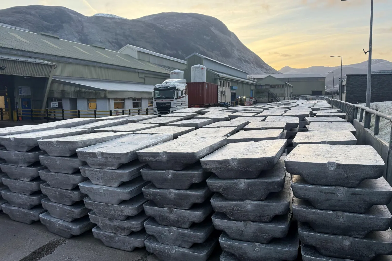 Alvance British Aluminium The metal is stacked in a yard. A heavy goods lorry and parts of the smelter plant, along with Ben Nevis, are in the background.
