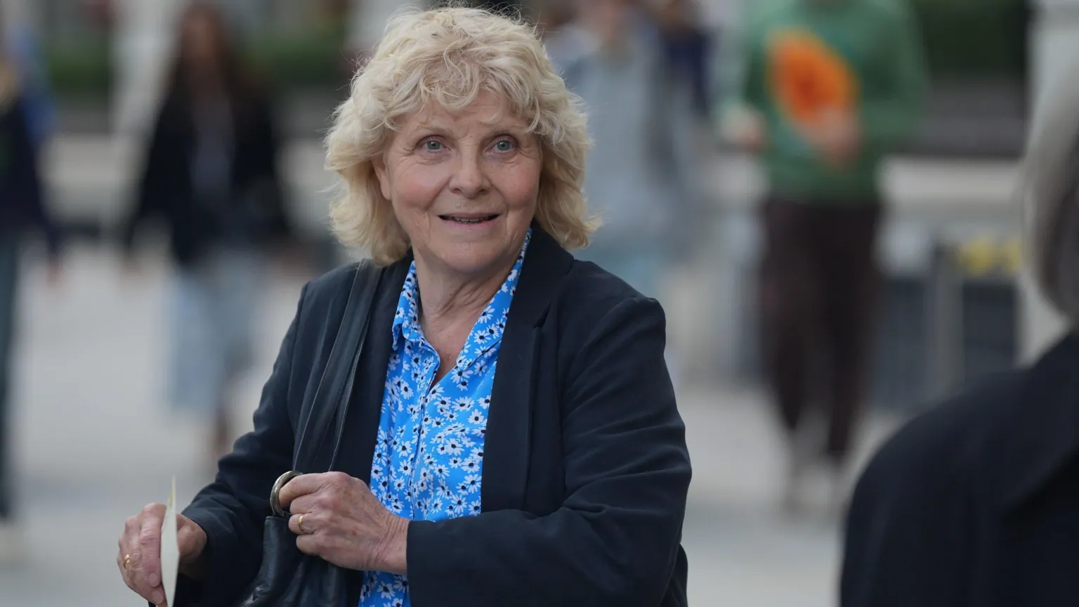 Jo Hamilton as photographed after leaving the Post Office Horizon IT inquiry in London in 2024. She is wearing a blue shirt with a floral pattern and a dark jacket and she has curly blonde hair.