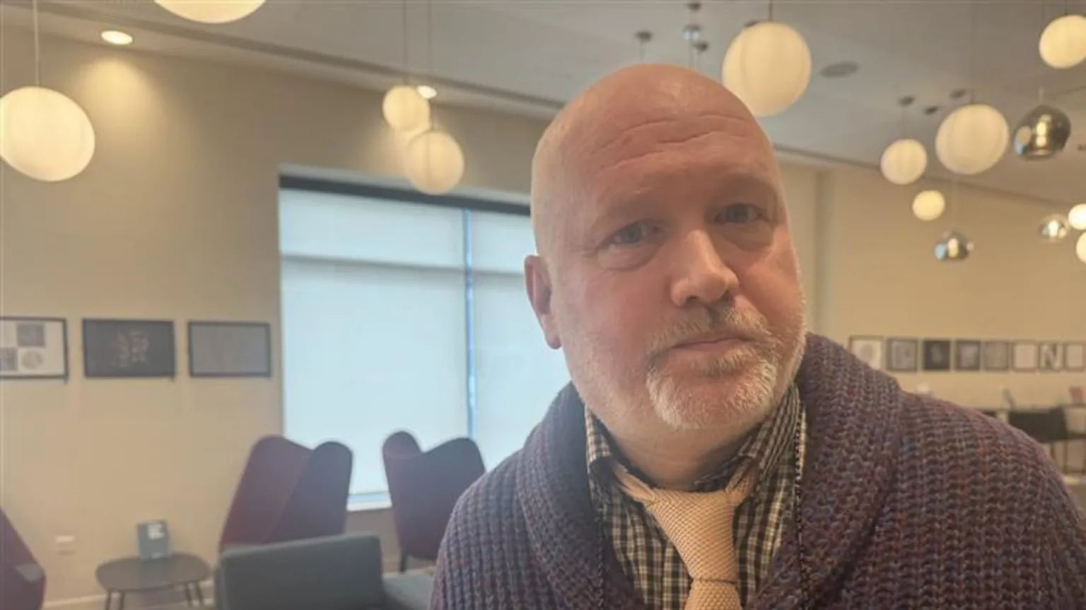 Head and shoulders shot of a man in Phoenix Cinema. He is bald and has a salt and pepper goatee. He is wearing a checked shirt, pink tie and brown cardigan.
