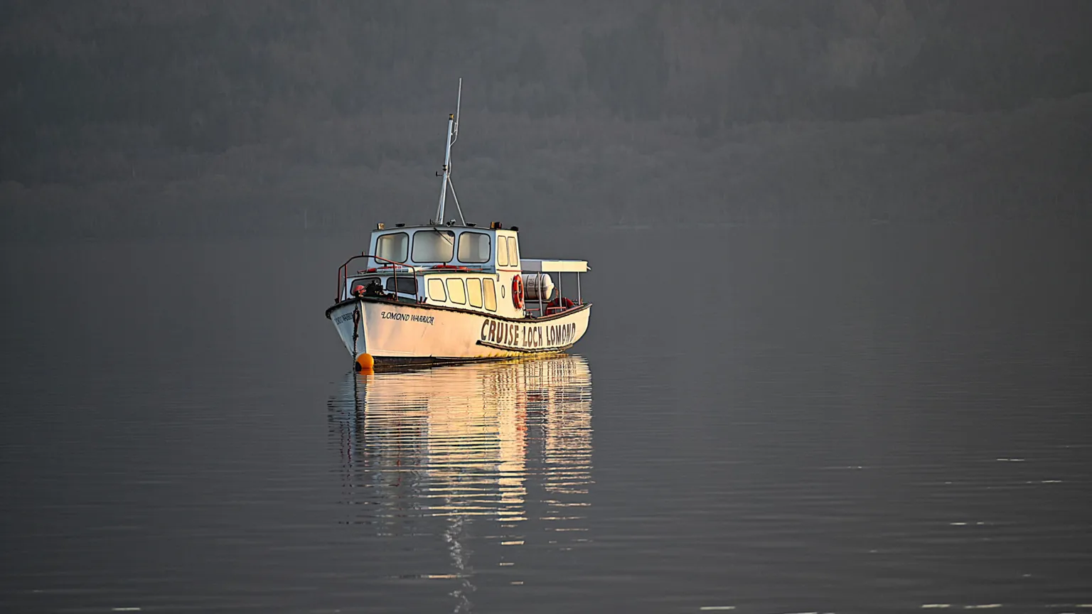 Victor Tregubov A small white boat sits still on calm, reflective water in soft evening light, with faint hills forming a dark backdrop.