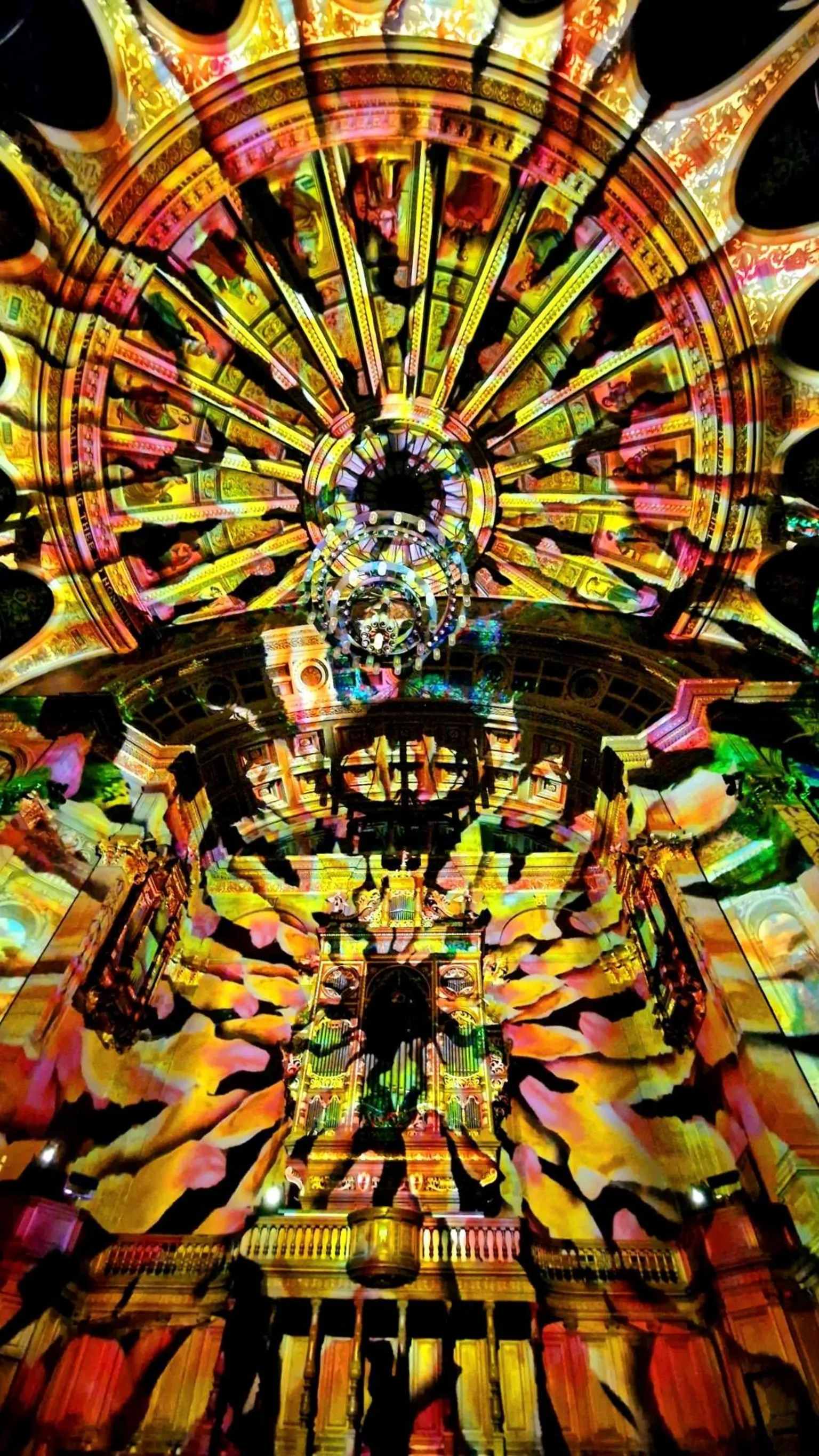 Janina Dolny A cathedral interior filled with vivid, multi-coloured light projections, creating swirling patterns across the domed ceiling and ornate architecture.