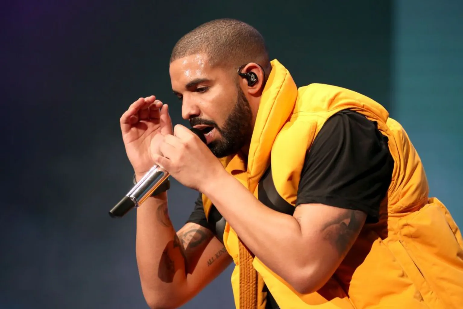 Drake performs on stage, wearing a yellow bomber jacket over a black t-shirt
