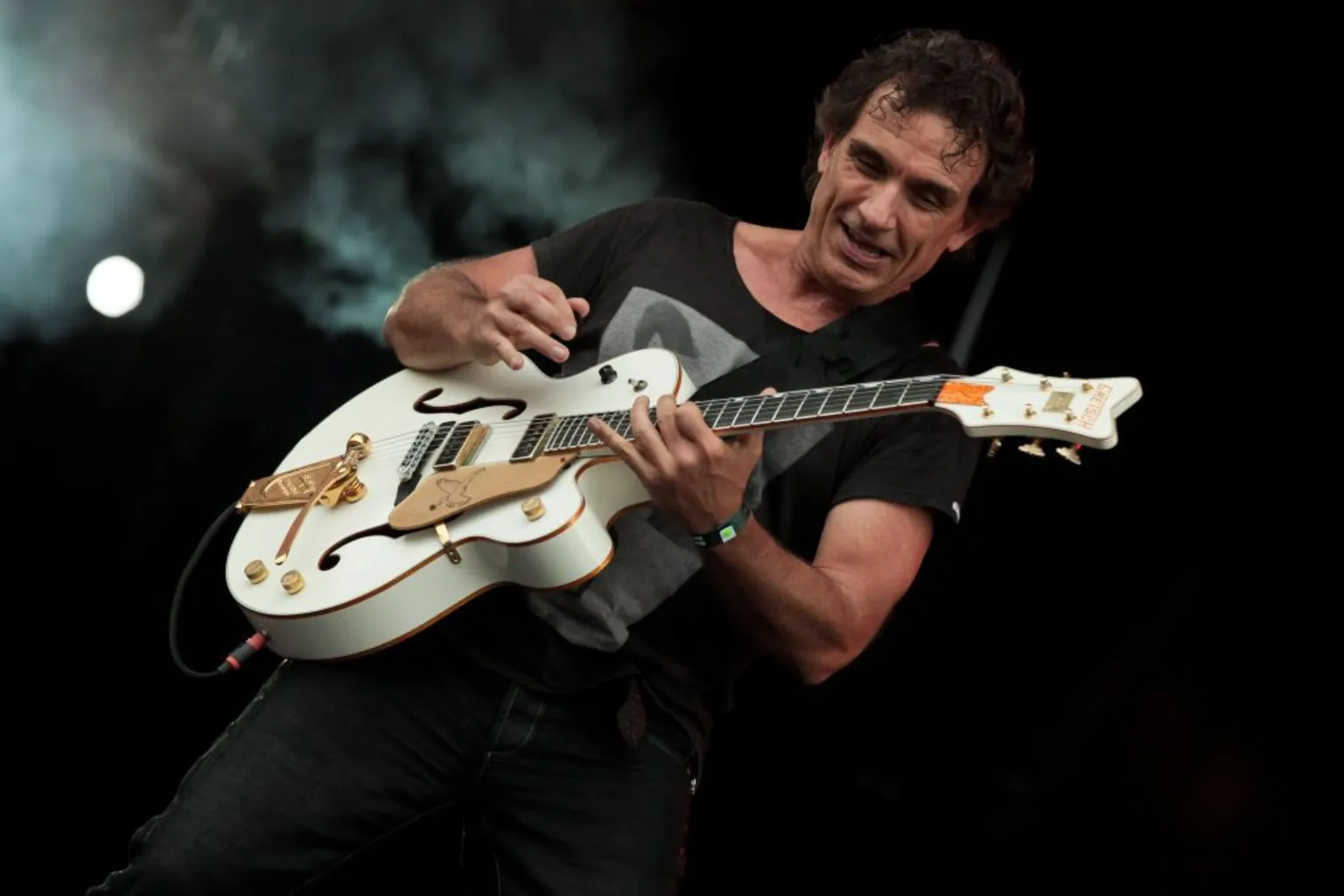 Ian Moss of Cold Chisel plays guitar against a moody black background