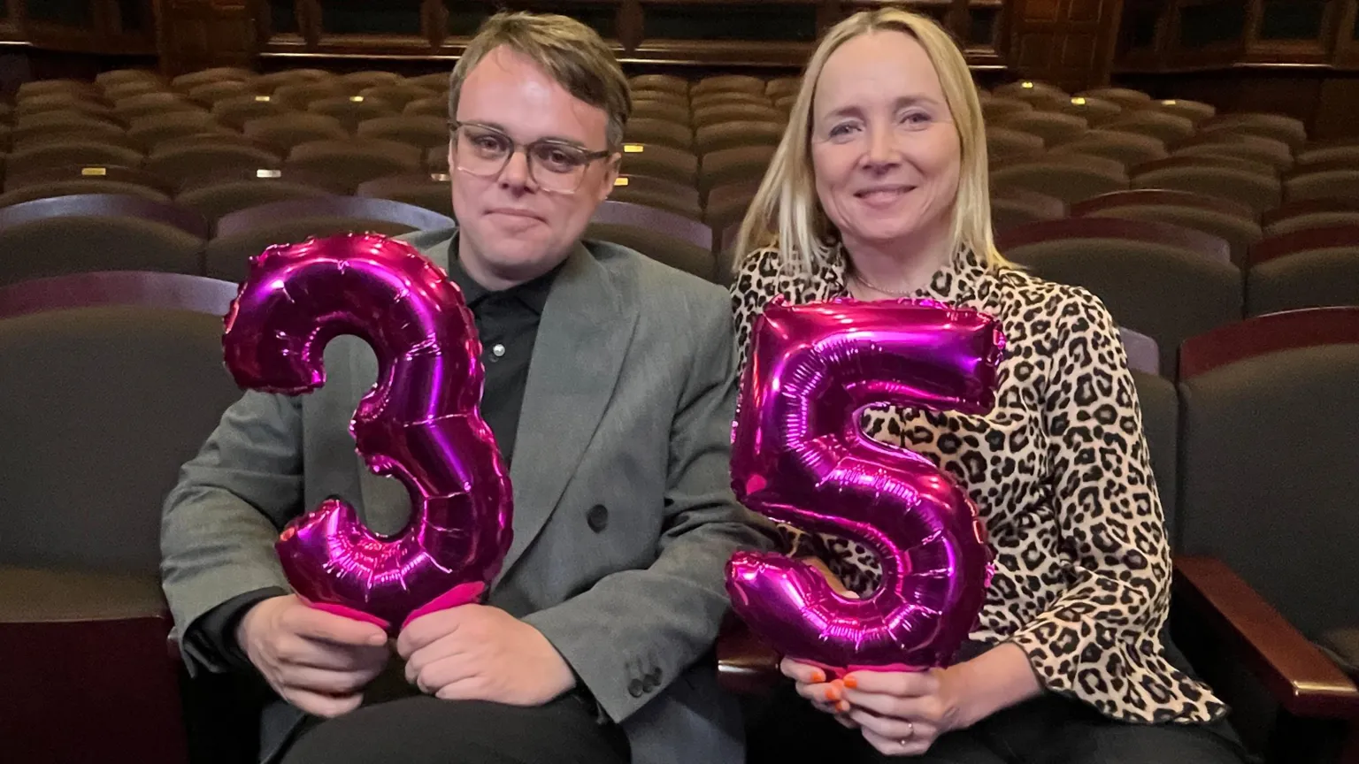 Pasha on left of screen holding pink 3 -- in grey jacket and black shirt and trousers Katie Razzall on right of screen holding pink 5 -- in leopard print blouse & dark trousers. Sitting in auditorium