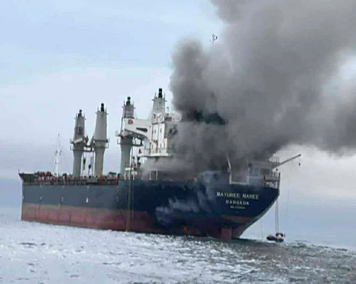 An oil tanker with thick grey smoke billowing from its stern