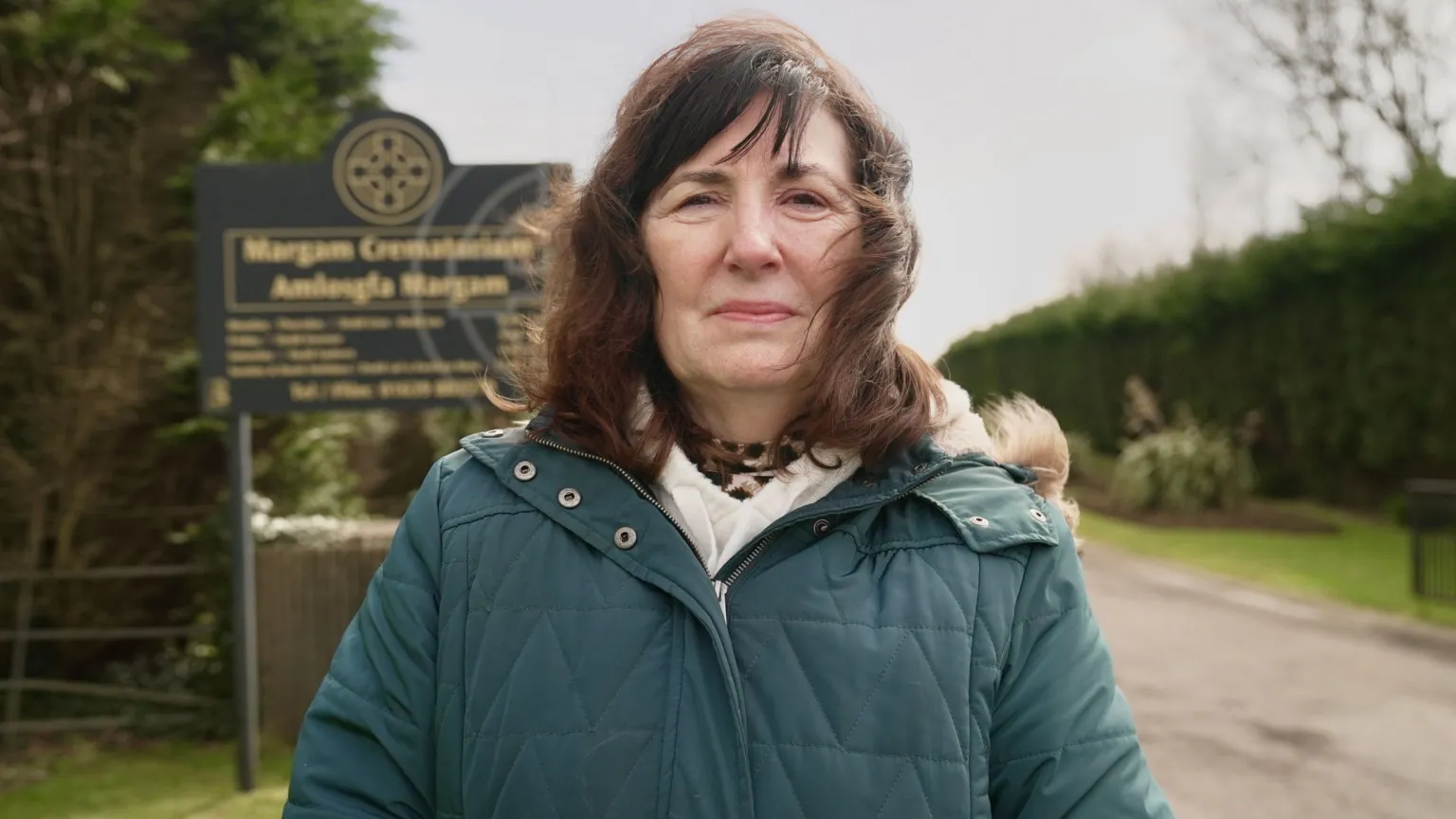 A woman dressed in a bluey grey anorak stands at the entrance to Margam Crematorium