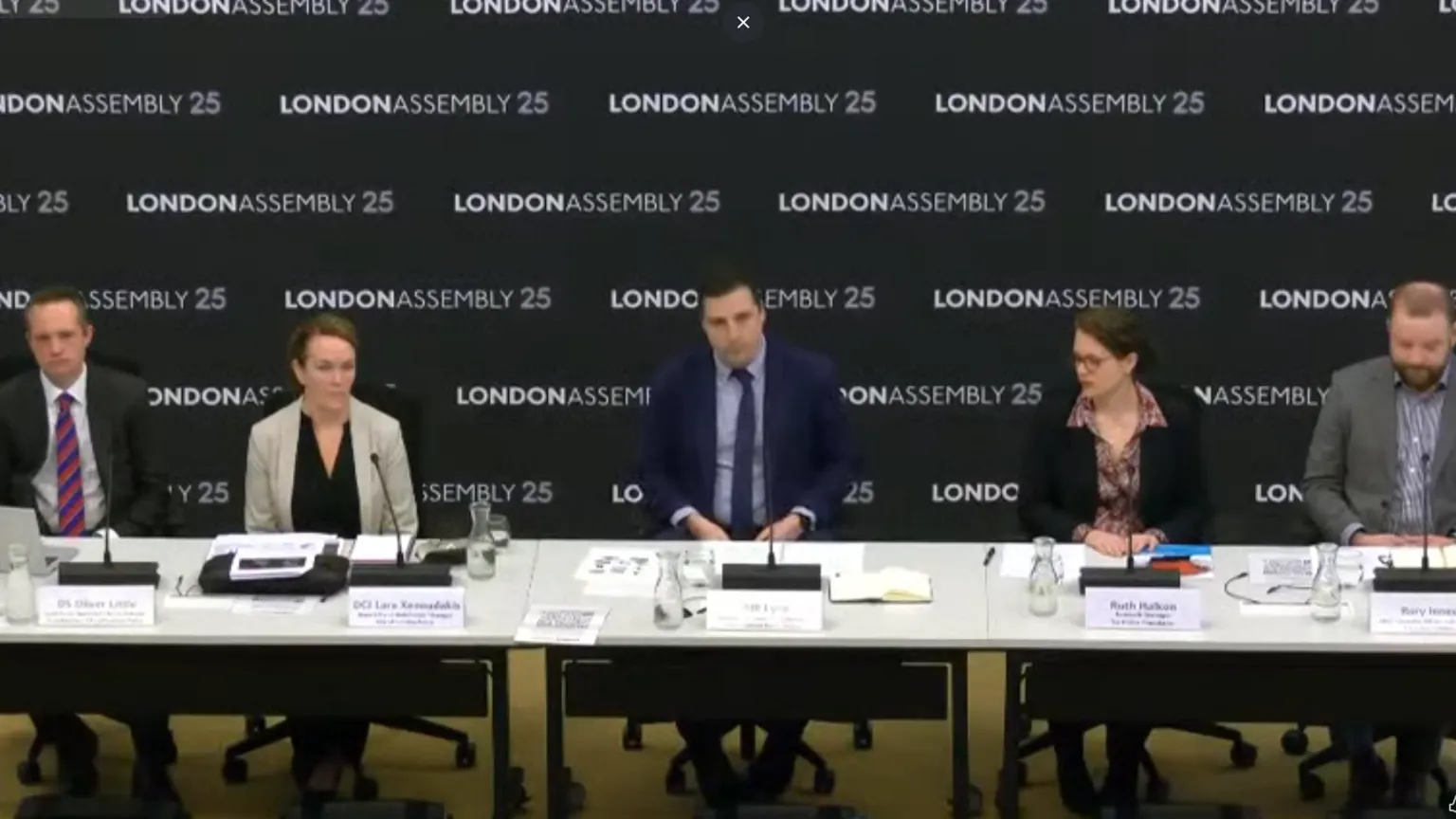 London Assembly Five panel members, including three men and two women, sit behind a row of desks at a meeting. Behind them is a backdrop that says London Assembly 25.