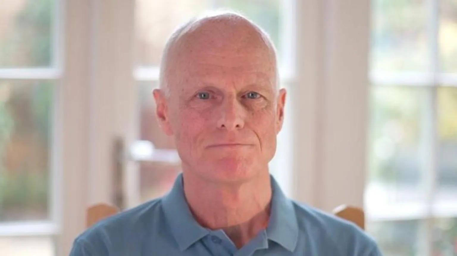 Jamie Niblock/BBC David Phillips has a shaved head and is wearing a blue polo shirt in front of windows.