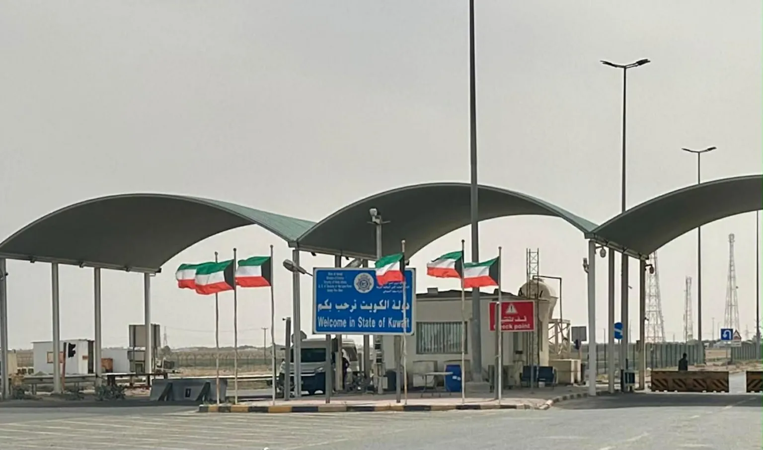Ross Slater A security checkpoint with black, green, white and orange flags and a sign that says Welcome In State of Kuwait