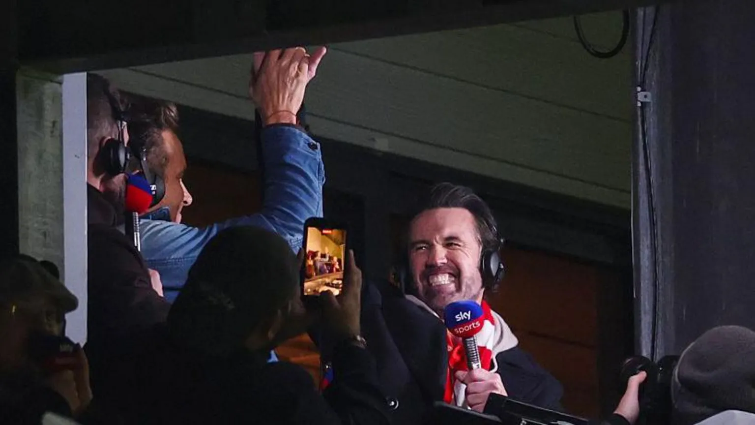 Rob and Ryan celebrating after Wrexham score. They are high fiving each other, whilst holding their commentary microphones and wearing headphones.