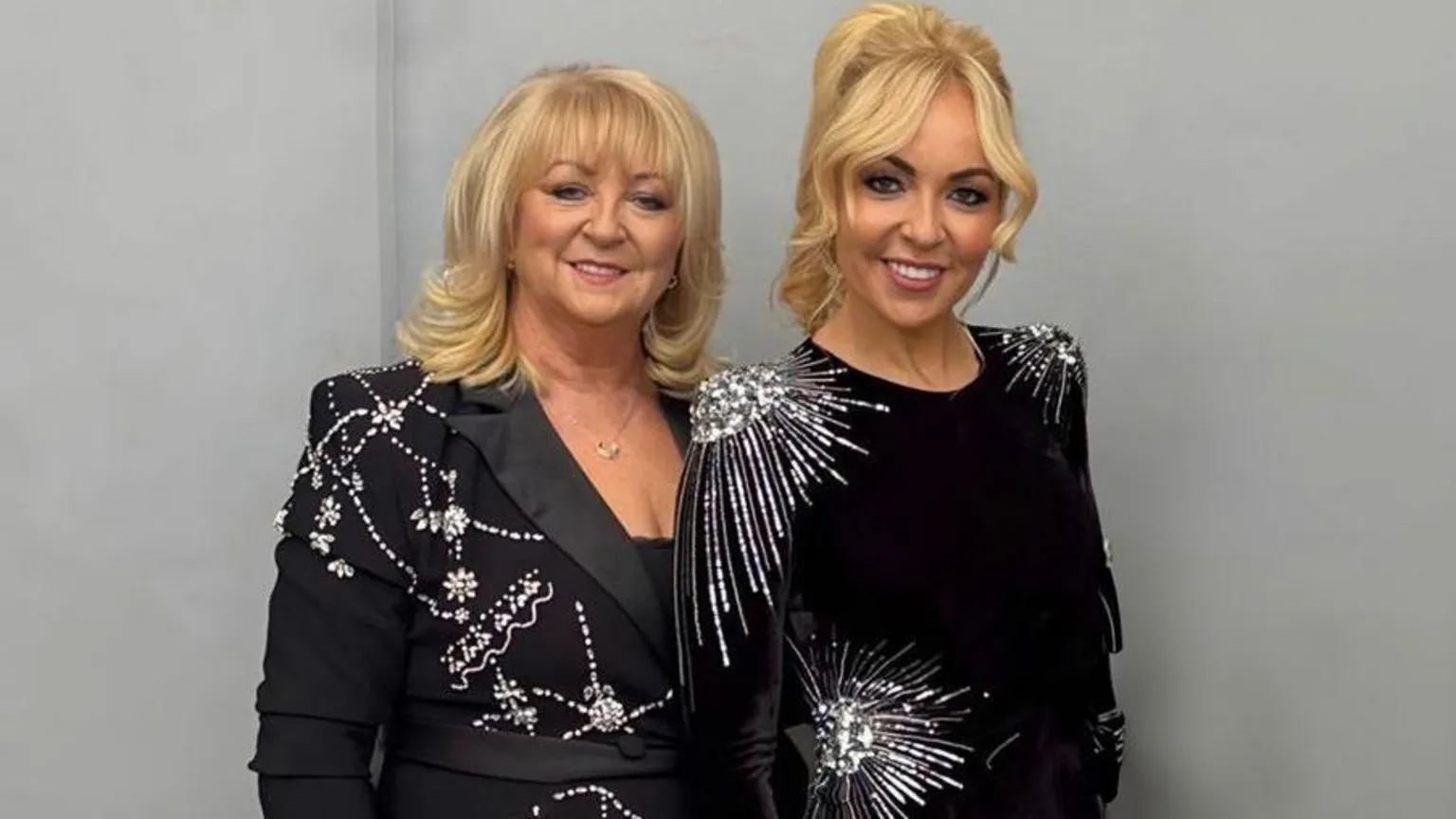 Chantelle Joseph Jane and Chantelle Joseph are standing side by side in front of a grey-painted wall. They are both wearing black dresses with silver embellishments.