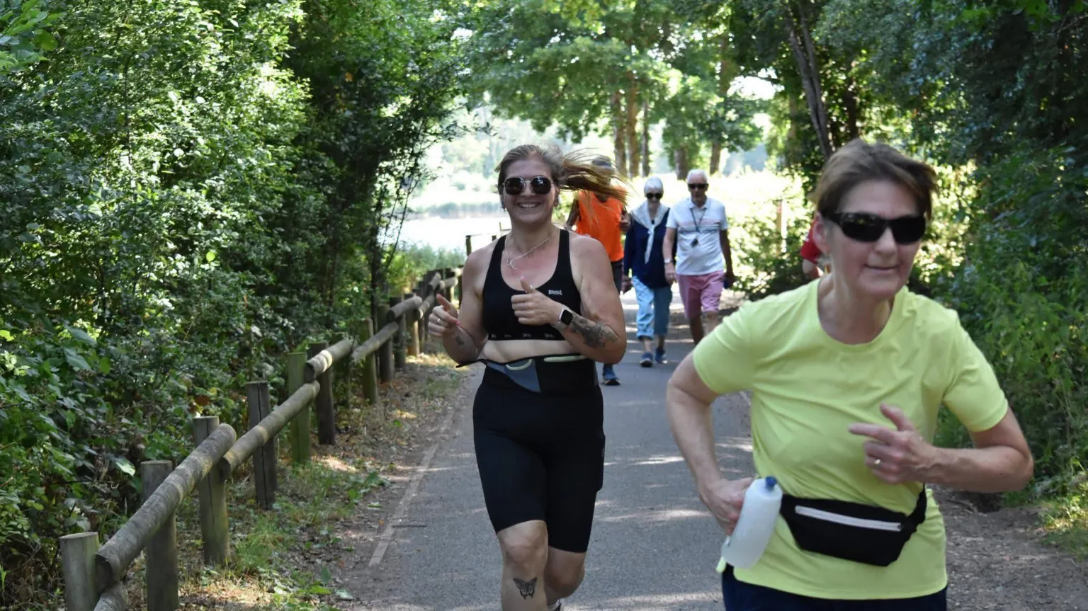Cat Byrne A woman runs along a path and smiles with her thumbs up at the camera. She wears running gear: a black crop top and black shorts.