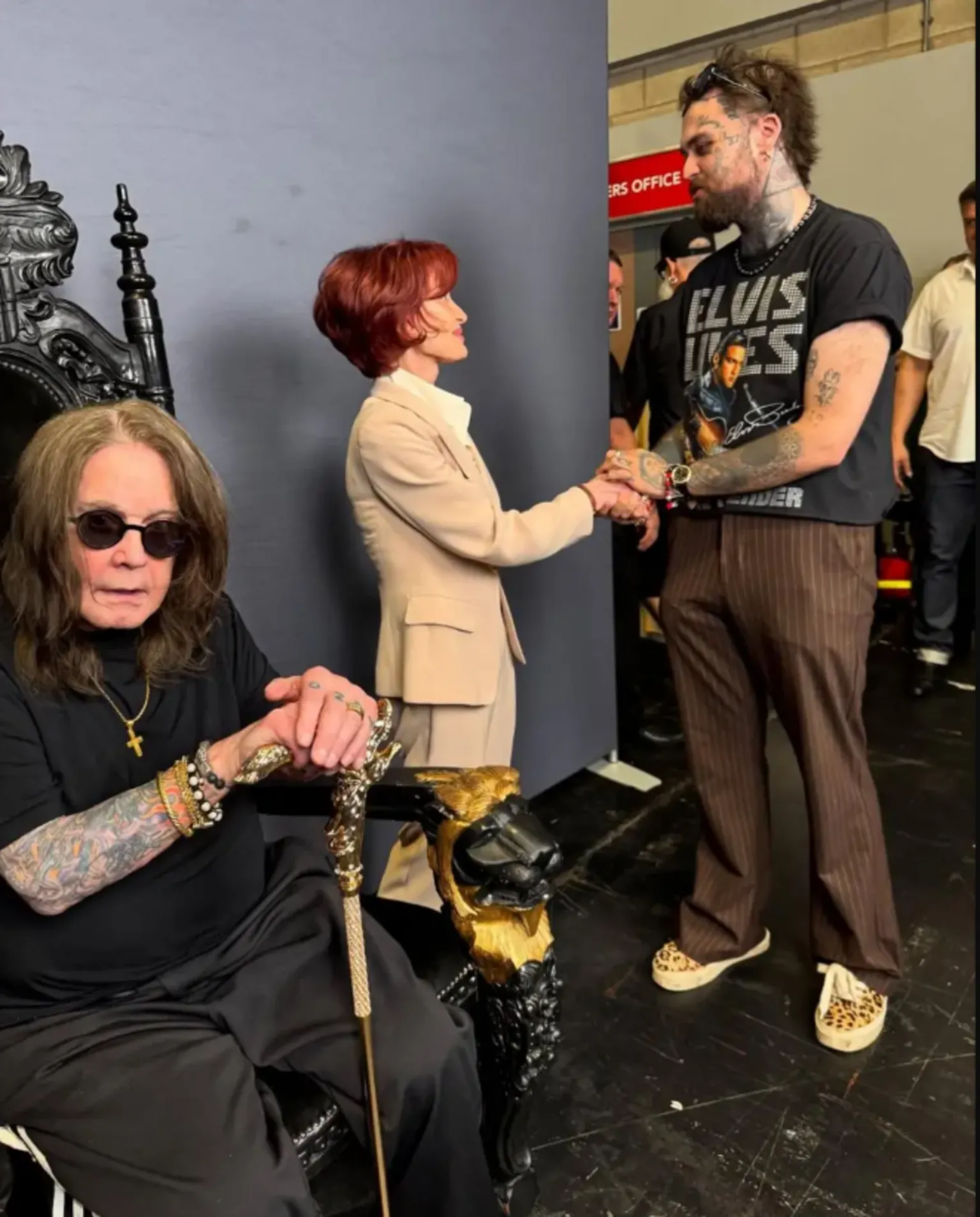 Mason Newman Mason, on the right, shakes Sharon Osbourne's hand as Ozzy sits in a chair in the foreground of the photo. Mason is wearing brown trousers and a black T-shirt. He has brown hair and a beard. Sharon is wearing a beige suit and Ozzy is dressed all in black and leaning on a cane.