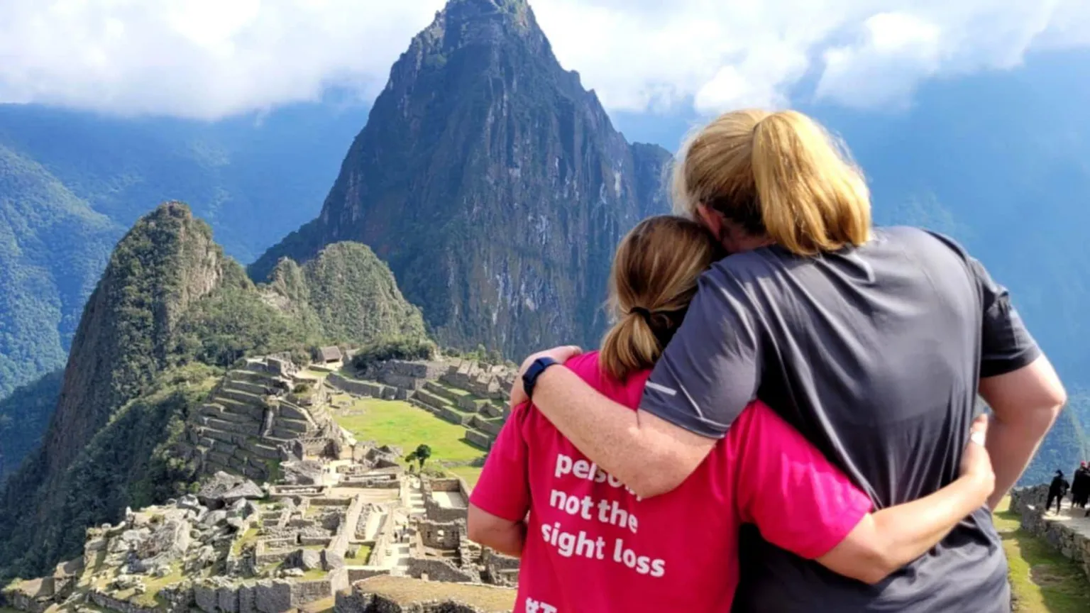 Cathie Rowe Cathie and Tricia facing outwards at Machu Picchu in Peru. The pair have their arms around one another as they look at the moutains in the distance.